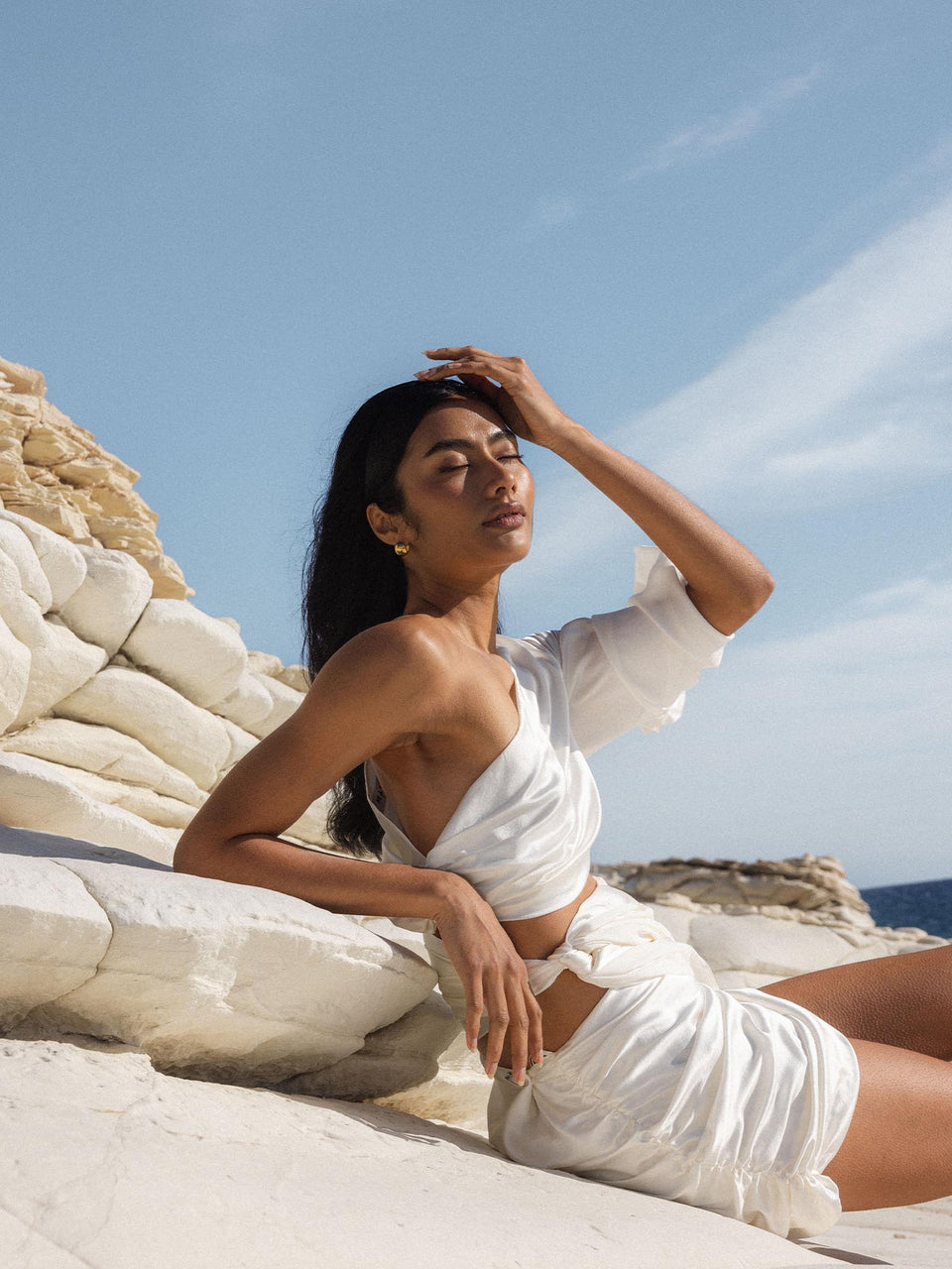 Leo Letter Charm 18K vergoldet am Ohr einer Frau vor sonnigem Strandhintergrund, elegante PURELEI Ästhetik