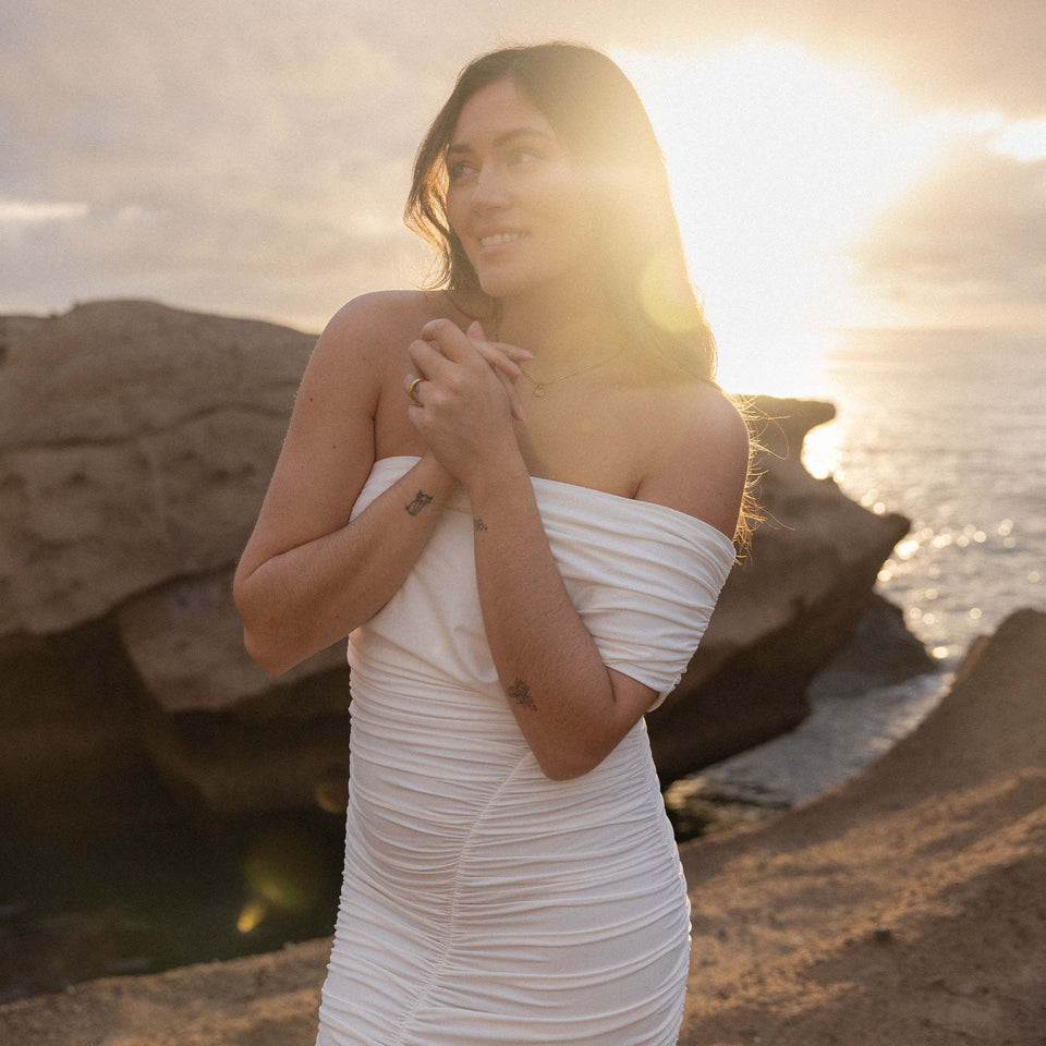PURELEI Geburtsstein Juli Rubin Charm in 18K Gold mit funkelndem Rubin, elegant im warmen Sonnenlicht am Strand.