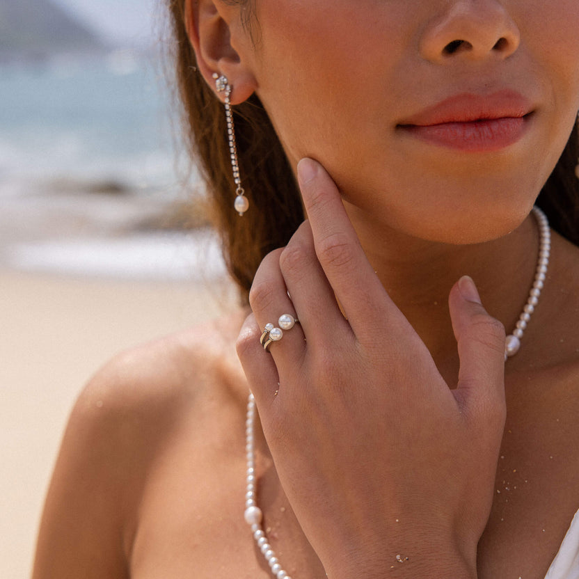 Elegante PURELEI Perlenohrringe und Ring, strahlend am Strand getragen.
