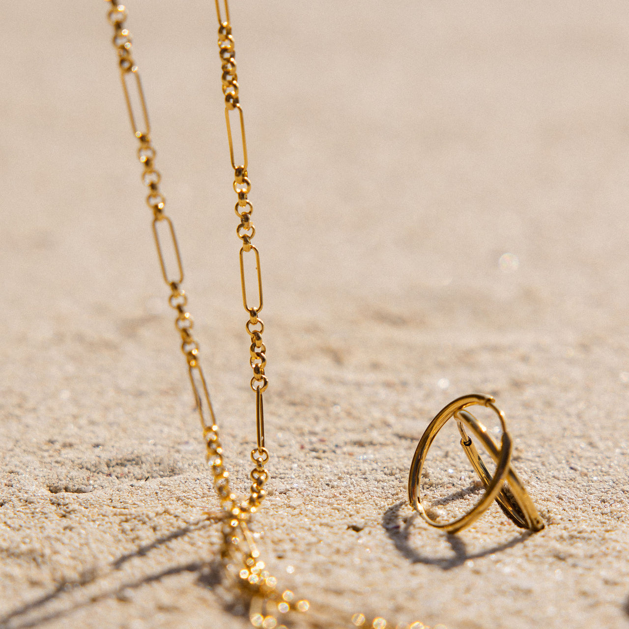Goldene PURELEI Unison Kette mit unterschiedlichen Gliedern, elegant auf Sand gelegen, feminine Leichtigkeit.