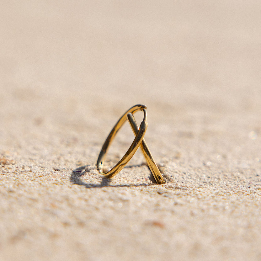 Zwei goldene Ringe im Sand, inspiriert von PURELEI, strahlen tropische Eleganz aus.
