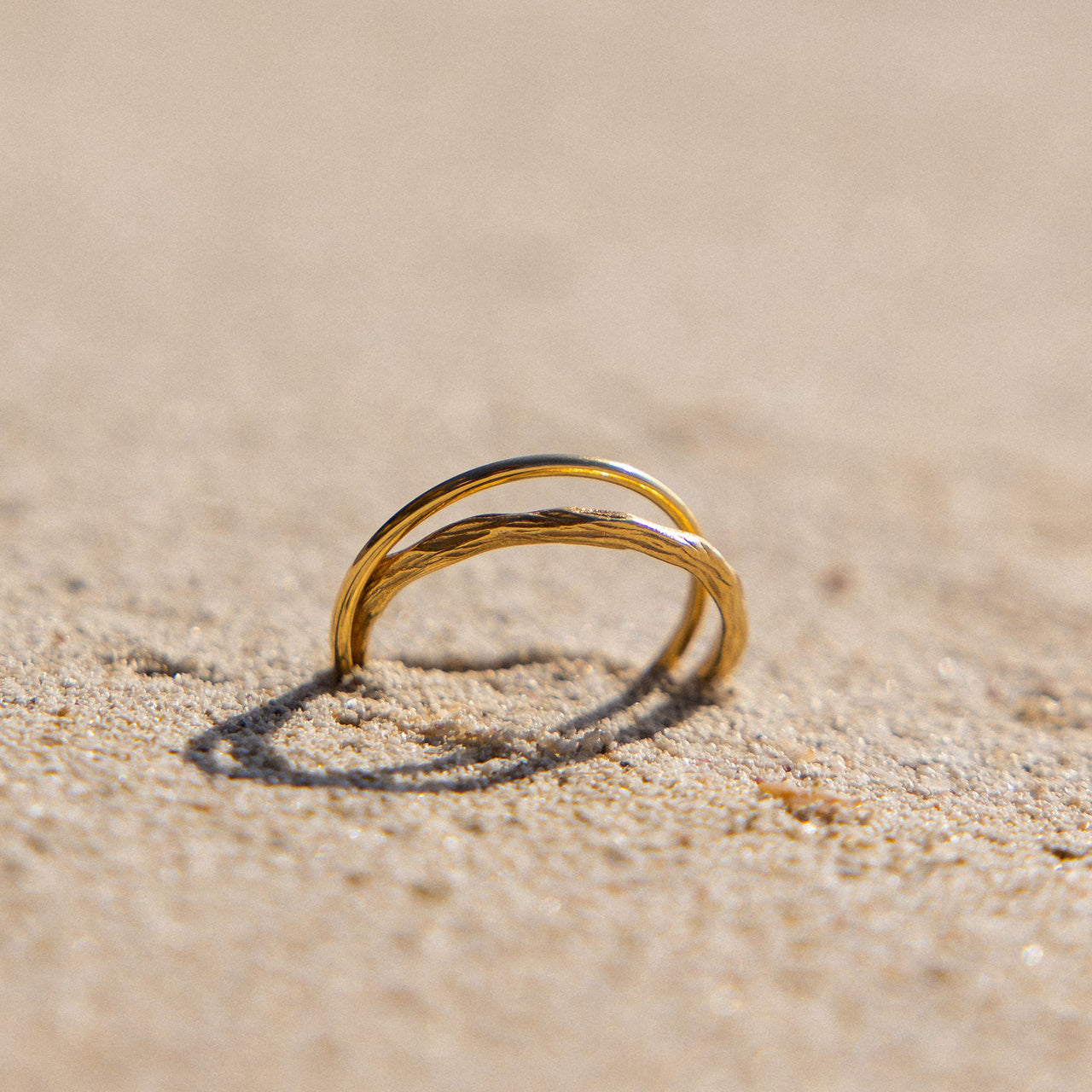 Double Match Anxiety Ring von PURELEI – 18K vergoldete, ineinander verschlungene Ringe im warmen Sand mit sonniger Leichtigkeit.