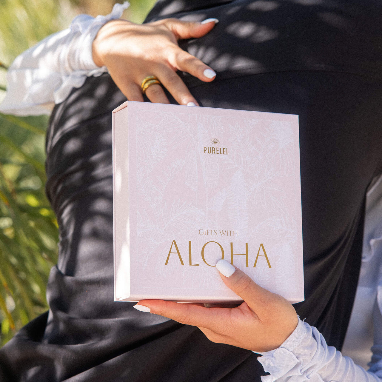 PURELEI Aloha Geschenkbox in zartem Rosé mit tropicalem Weißblattprint und goldveredelter Schrift, elegant und wiederverwendbar.