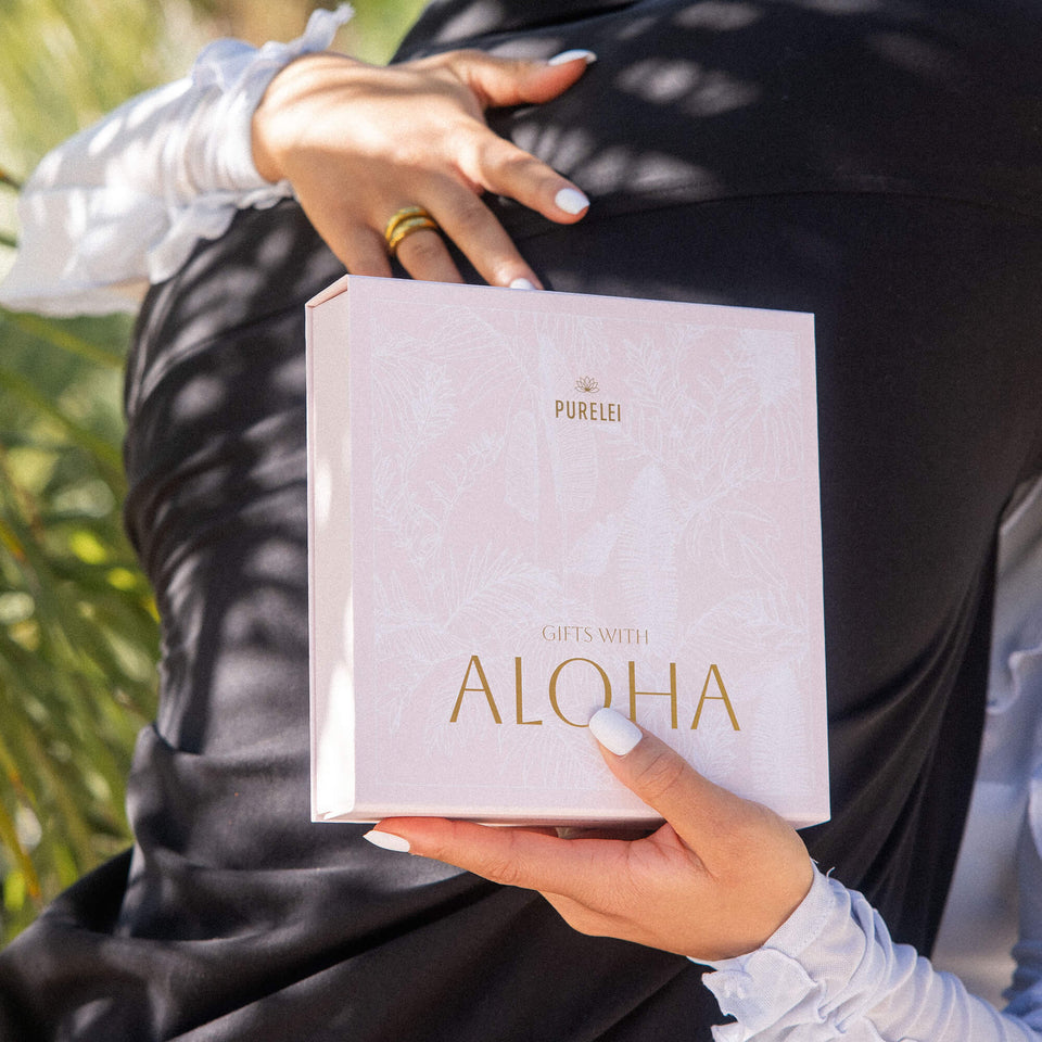 PURELEI Aloha Geschenkbox in zartem Rosé mit tropicalem Weißblattprint und goldveredelter Schrift, elegant und wiederverwendbar.