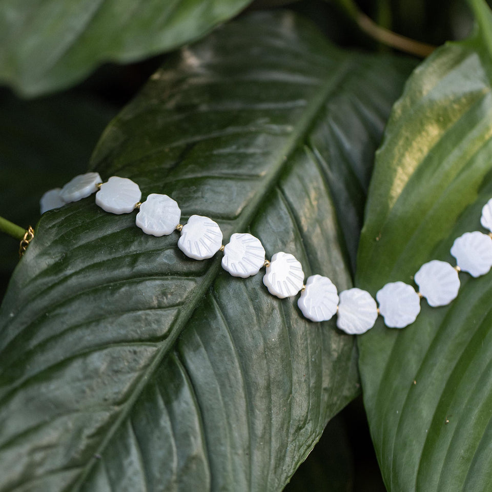 PURELEI White Sparkle Kette mit goldenen Muschelperlen auf grünem Blatt, elegant und naturverbunden.
