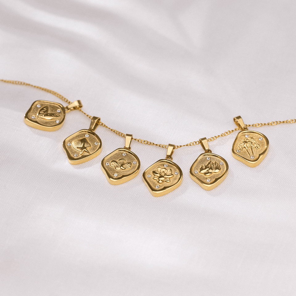 Volcano Coin Charm aus 18K Gold, asymmetrischer Anhänger mit Vulkanmotiv und funkelnden Zirkonia-Steinen auf weißem Stoff.