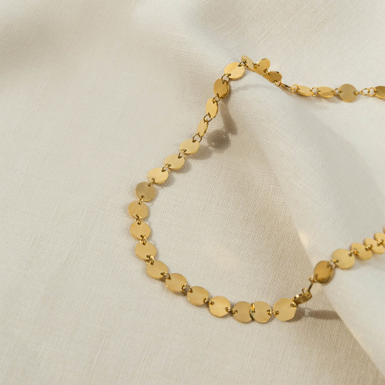 PURELEI Kalani Kette aus goldenem Edelstahl mit feinen Plättchen auf hellem Stoff, elegant und leicht tragbar