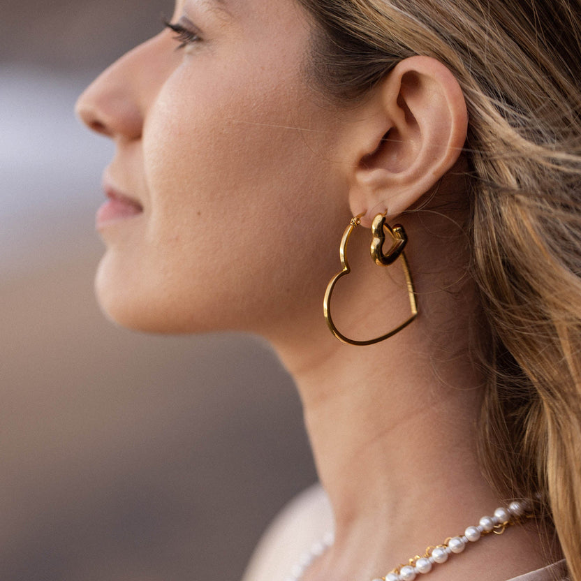 PURELEI Big Love Ohrringe aus 18K Gold vergoldetem Edelstahl, herzförmig, feminine Leichtigkeit am Strand getragen.