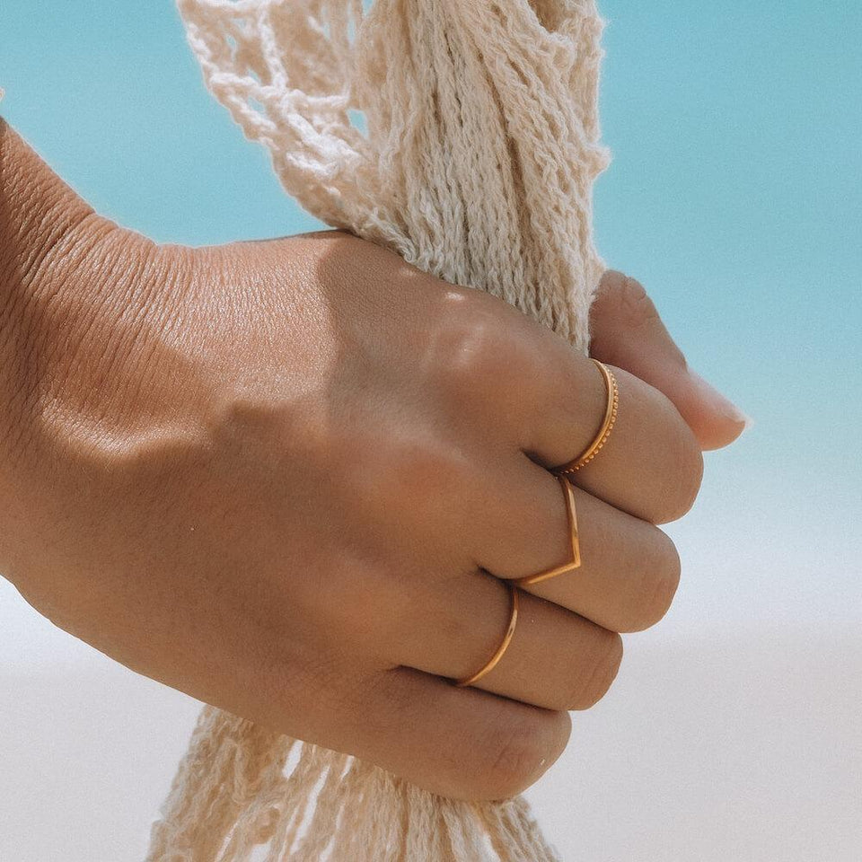 Lihini Ring von PURELEI, 18K vergoldeter Edelstahl, minimalistisch, am Hand gehalten vor blauem Himmel, elegant und feminin
