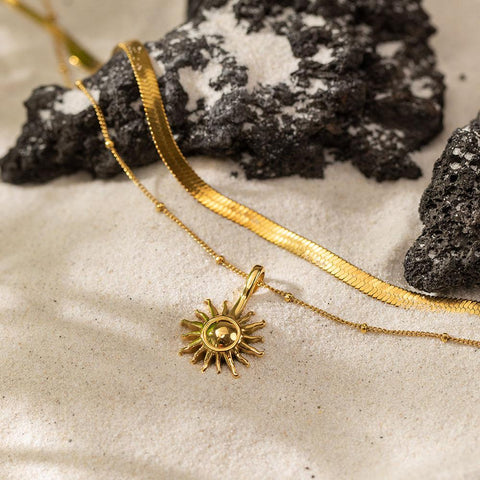 Molokai Ketten-Set von PURELEI, goldene Edelstahlketten mit Sonnenanhänger, elegant auf hellem Sand arrangiert.