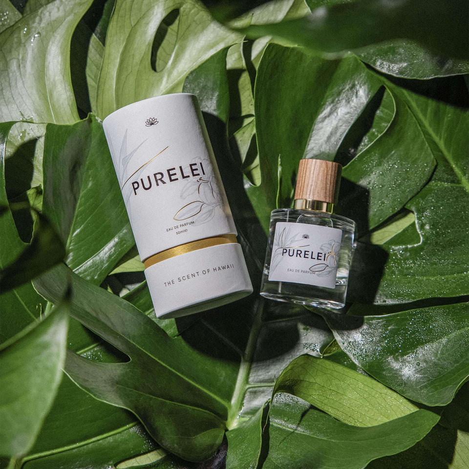 PURELEI Eau de Parfum in Glasflakon mit Holzdeckel, umgeben von saftig grünen Blättern, tropisch und frisch