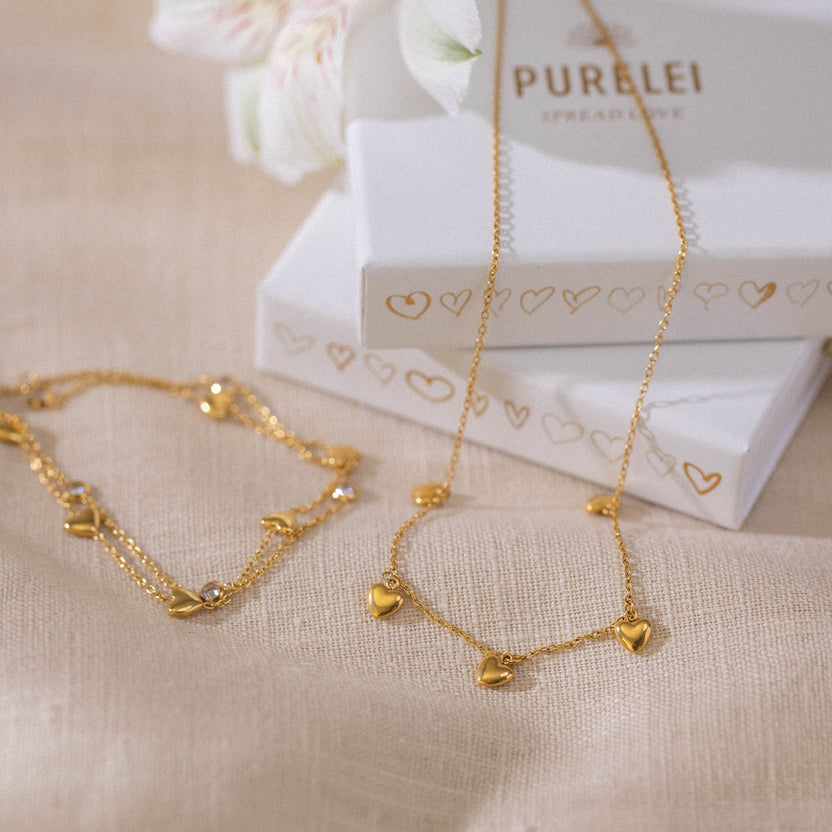 Goldene Kette und Armband mit Herzanhängern, elegant auf Leinen präsentiert – PURELEI.