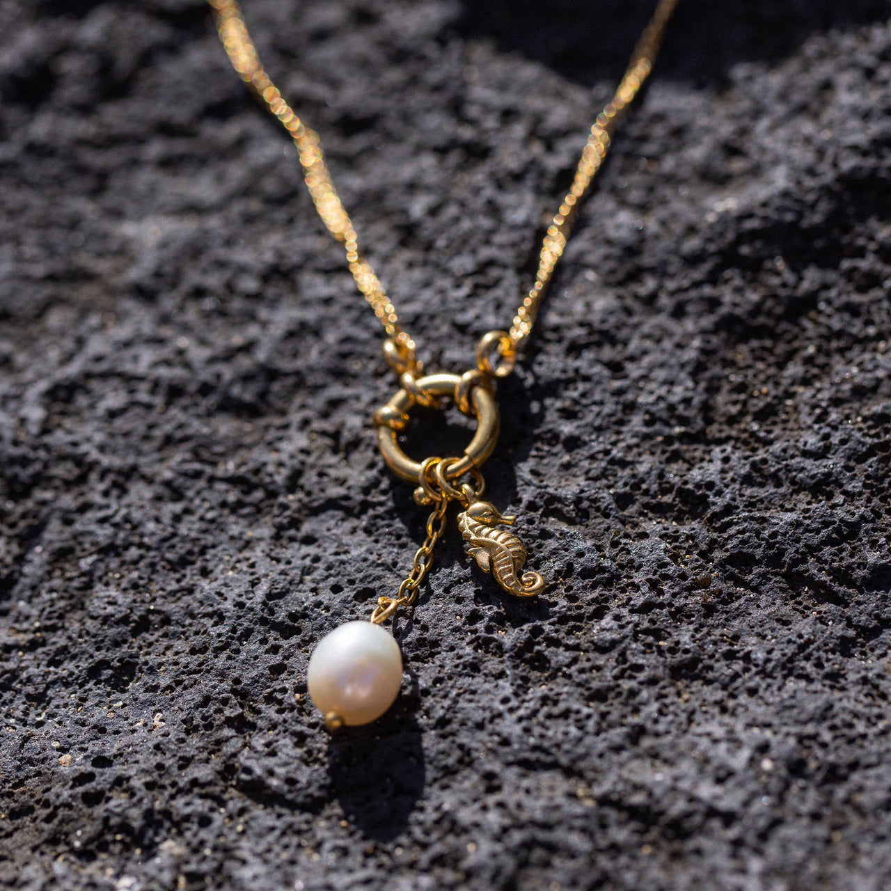 Seahorse Charm von PURELEI, vergoldet mit Perlenanhänger auf vulkanischem Gestein, elegant und feminin.