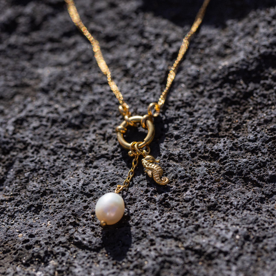 Seahorse Charm von PURELEI, vergoldet mit Perlenanhänger auf vulkanischem Gestein, elegant und feminin.