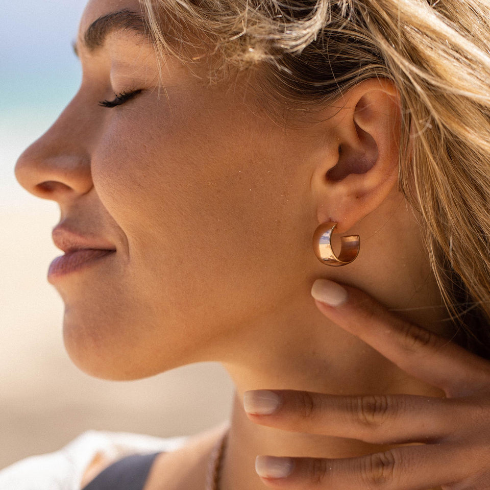PURELEI Bold Ohrringe aus rosévergoldetem Edelstahl, breite Creolen, feminine Eleganz am Strand getragen.