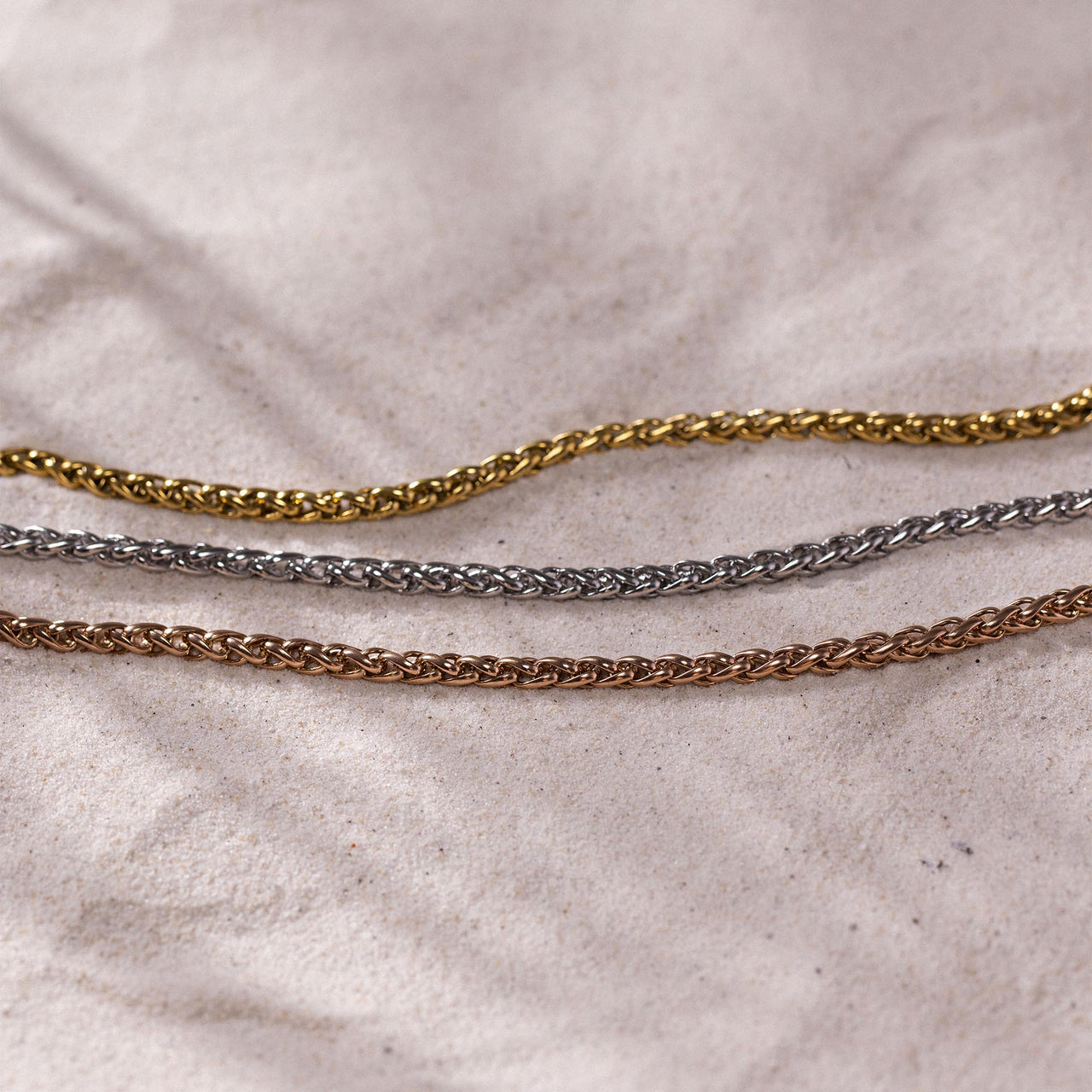 Dreifache Twisted Bold Kette aus vergoldetem, silbernem und roségoldenem Edelstahl auf sandigem Stoff PURELEI.