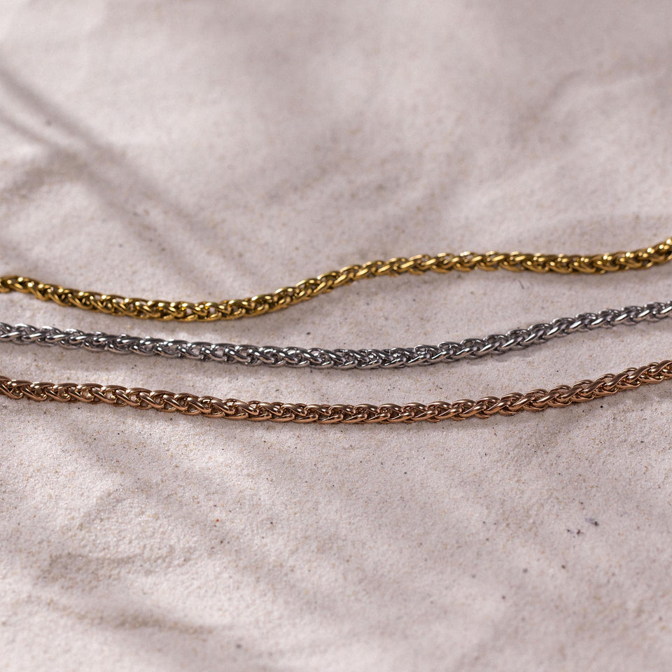 Dreifache Twisted Bold Kette aus vergoldetem, silbernem und roségoldenem Edelstahl auf sandigem Stoff PURELEI.