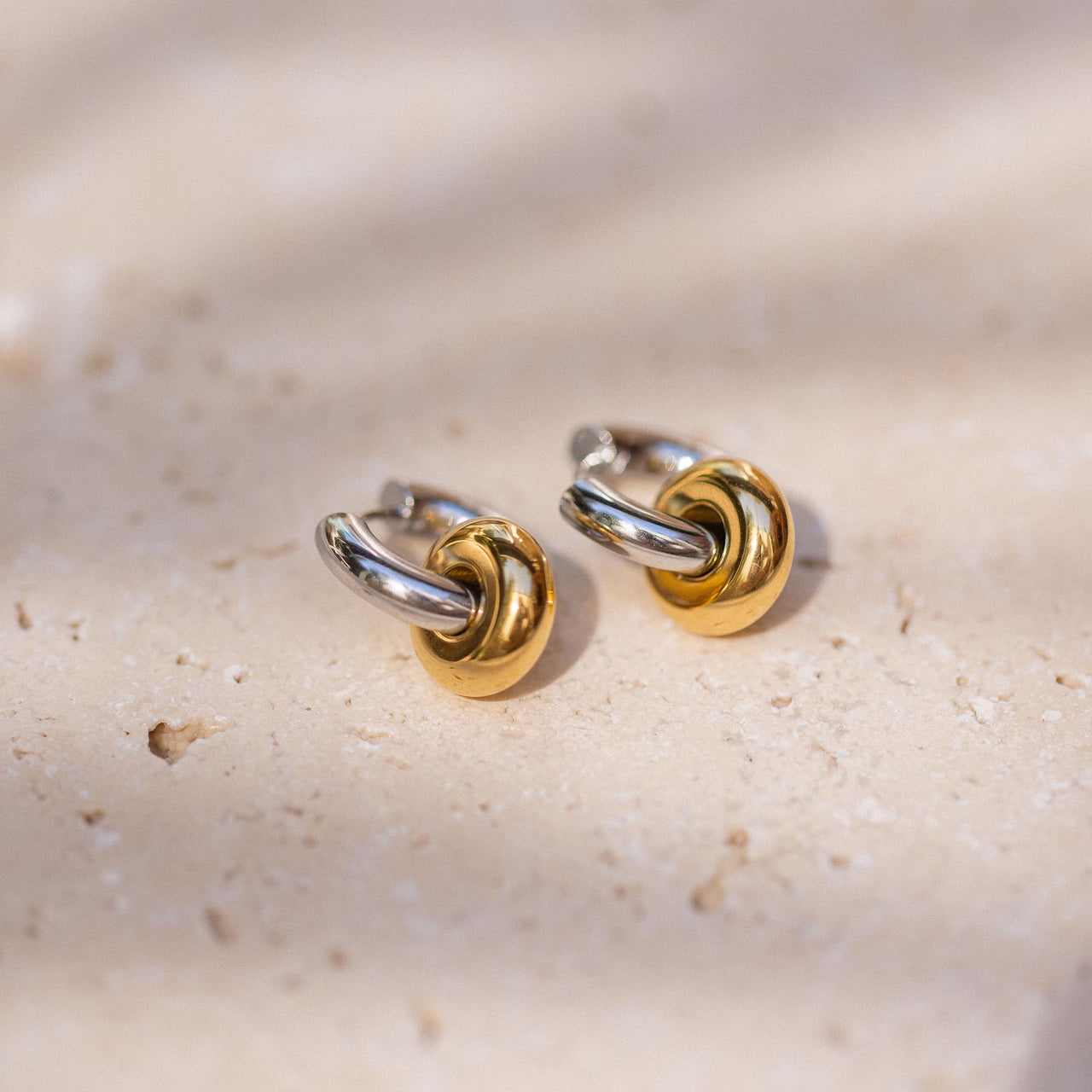 PURELEI Bond Ohrringe in Bicolor aus Gold und Silber, elegante Creolen mit knotigem Design auf hellem Stein.