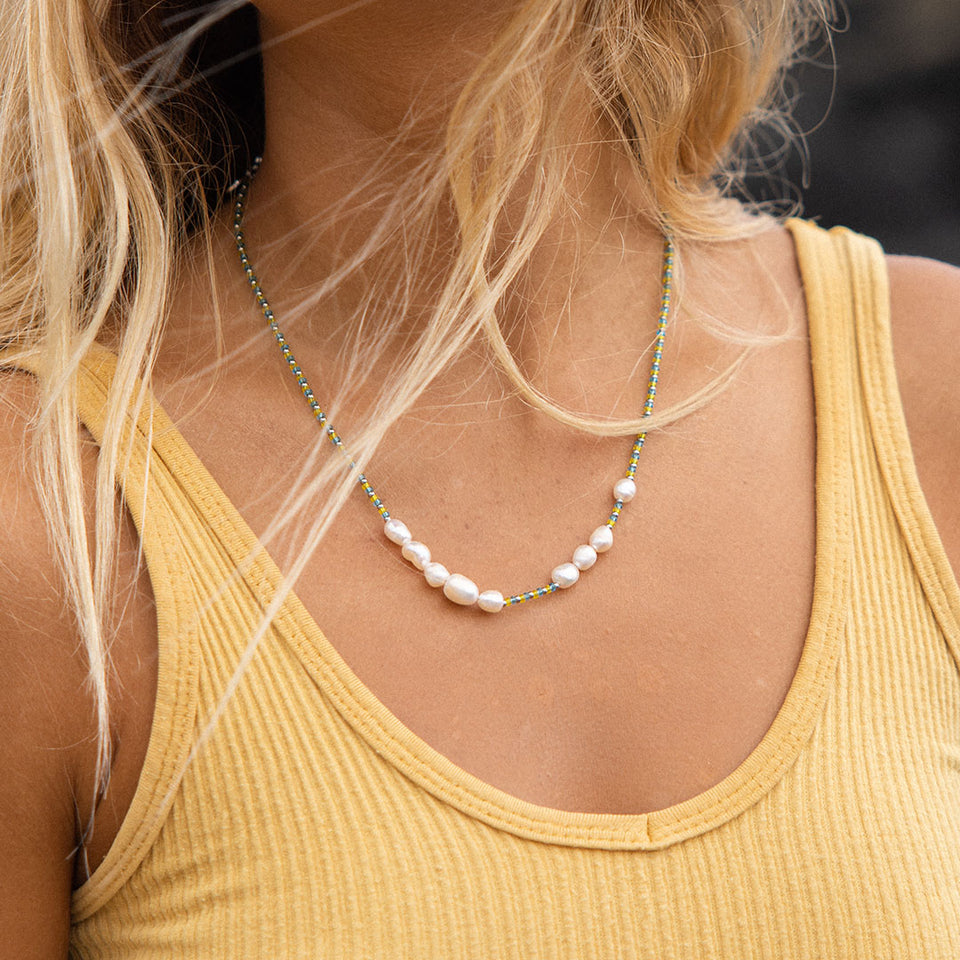 Blissful Kette von PURELEI mit goldfarbenen Perlen und blau-gelbem Perlenmix, sommerlich und elegant getragen.