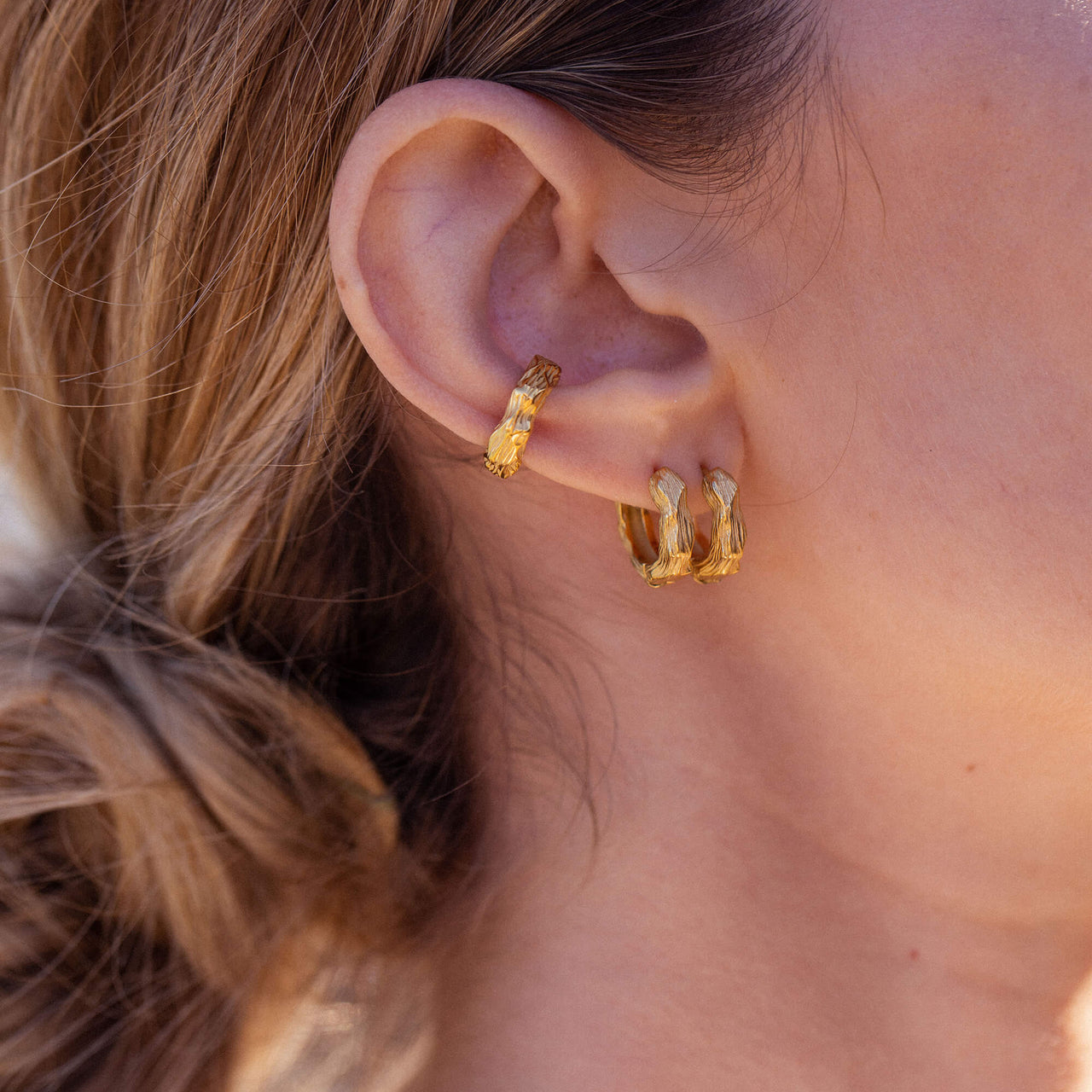 PURELEI Brushed Ohrringe aus 18K Gold, gehämmert, warmes Licht, minimalistisch und elegant am Ohr getragen.