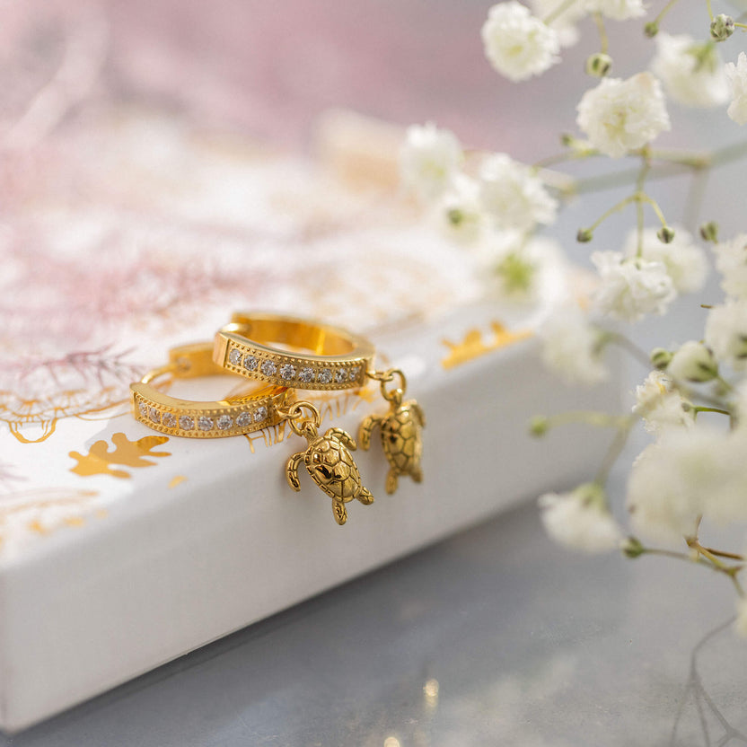 Goldene Ohrringe mit Schildkröten-Anhängern von PURELEI, elegant und verspielt.