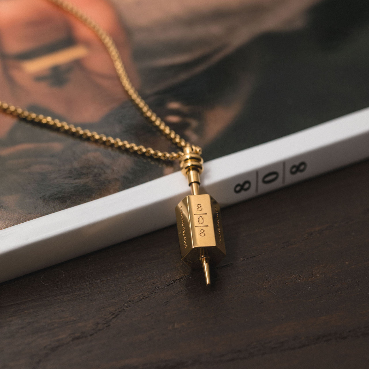 Goldene PURELEI 808 Kette aus Edelstahl mit graviertem Anhänger, elegant und modern inszeniert auf dunklem Holztisch.